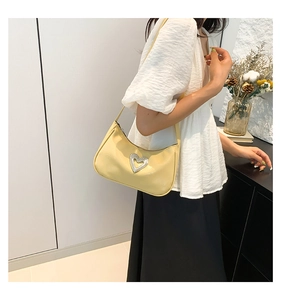 Detail of a creamy leather underarm bag with a rhinestone heart on a female model
