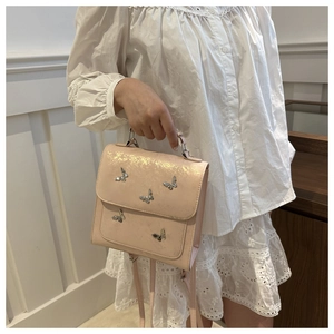 Detail of light pink metallic butterfly bag with silver charms on adjustable strap