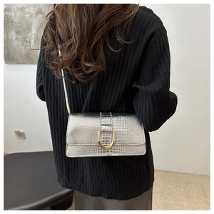 Détail du sac bandoulière argenté à motif crocodile avec boucle dorée sur un mannequin
