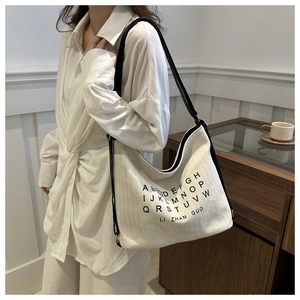 Close-up of cream canvas tote bag featuring black alphabet print and contrast straps