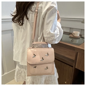 Detail of light pink shoulder bag featuring silver butterfly charms and top handle design