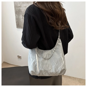 Detail of light gray pleated tote bag with silver chain worn by a model in a minimalist setting