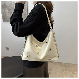 Detail of cream tote bag featuring silver butterfly studs and metal chain strap on model