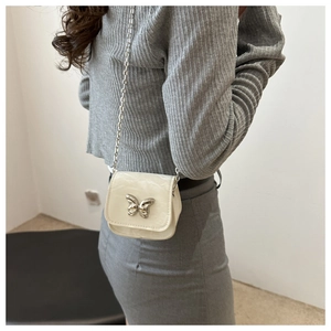 Close-up of mini off-white crossbody bag with silver butterfly buckle and chain strap