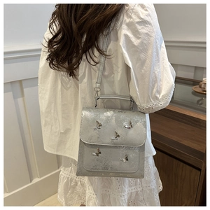 Detail view of silver crossbody bag featuring decorative metallic butterflies and top handle