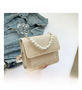 Detail of beige straw crossbody bag featuring pearl handle and gold-tone hardware accents