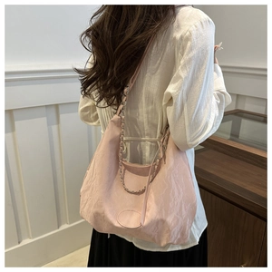 Detail of pink dumpling bag with pleated texture and metal chain worn by a model