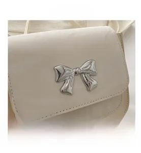 Detail shot of the cream crossbody bag featuring a polished silver metal bow buckle clasp