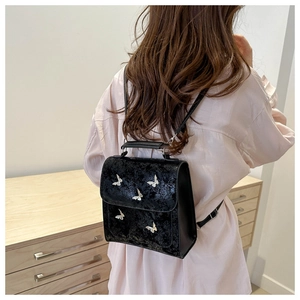 Detail of black backpack with silver butterflies on cracked leather worn by a model
