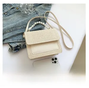 Detail of hand-woven straw bag with pearl handle on denim jacket for summer outfit