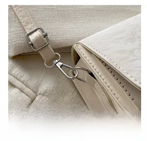 Detail of silver metal hook and adjustable leather strap on cream crossbody bag