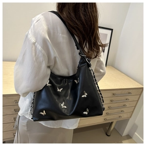 Detail of black butterfly tote bag showing silver metallic charms and leather strap texture