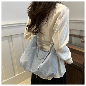 Detail of light blue wrinkled tote bag with silver chain strap shown on model's shoulder