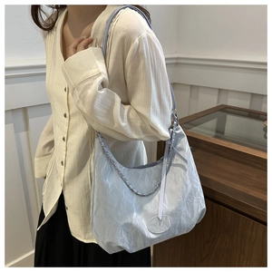 Light blue pleated nylon tote bag with silver chain detail on model in elegant interior