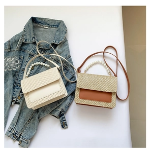 Detail of summer straw handbag with large pearl handle and faux leather trim on denim