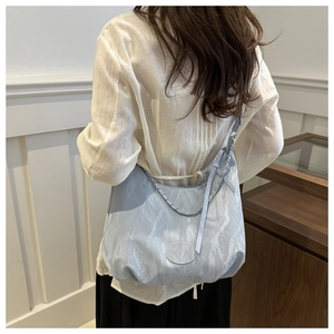 Detail view of light blue hobo bag with textured fabric, chain strap and ribbon decoration
