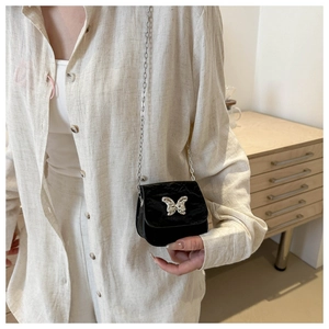Detail of a mini black velvet crossbody bag with a silver butterfly and chain strap
