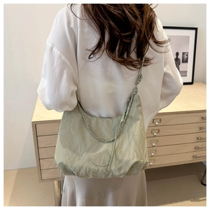 Close-up of light green crescent tote bag with pleats and woven handle on shoulder