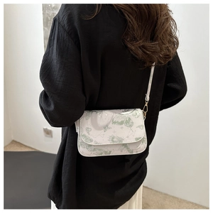 White crossbody square bag with green butterfly print shown on shoulder against a white wall