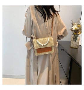 Detail of woven straw handbag with pearl handle and brown leather pocket detail