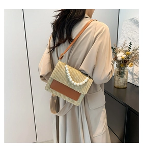 Straw crossbody bag with pearl handle and brown leather flap shown on model