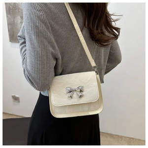 Détail du sac bandoulière blanc crème avec nœud en métal et texture cuir plissé