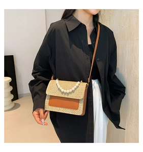 Detail of summer straw crossbody bag featuring pearl handle and brown leather flap