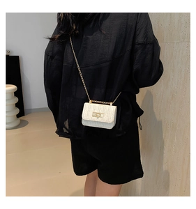 Detail of cream woven mini bag showing gold chain strap and rotary metal lock