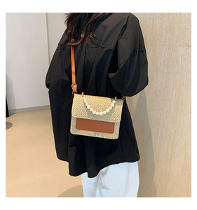 Detail view of woven straw crossbody bag featuring pearl handle and brown leather accents