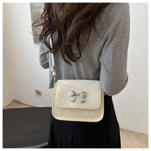Detail of cream white crossbody bag featuring texture grain and silver bow buckle ornament