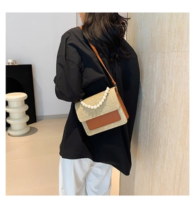 Detail of straw crossbody bag with pearl handle and leather flap worn by model