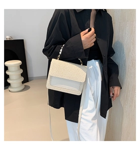 Detail of woven straw bag with faux pearl handle and white leather flap on woman