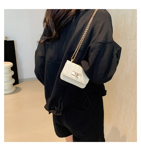 Detail of a mini straw crossbody bag with golden chain strap and metal lock closure