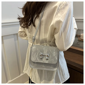 Détail du sac bandoulière en cuir verni argenté avec nœud métallique et texture plissée