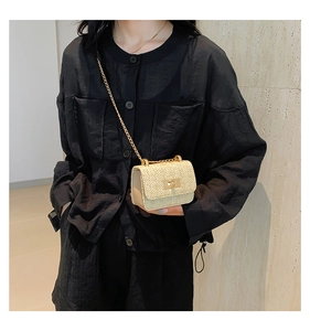Detail of hand-woven straw crossbody bag with golden chain and metallic turn-lock closure