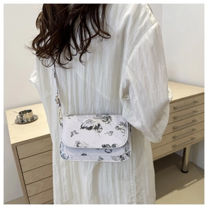 Detail of white butterfly print crossbody bag with gold hardware worn by a model