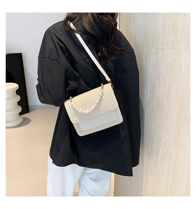 Detail of hand-woven crossbody bag with pearl handle worn by a model in a modern room