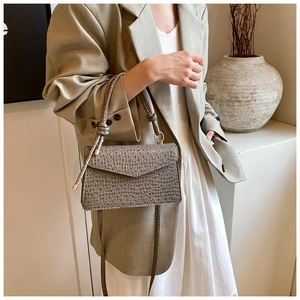 Close-up of grey crocodile-textured leather handbag with knot handle detail on model