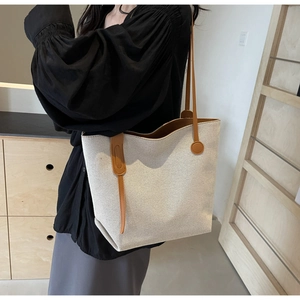 Close-up of minimalist canvas tote bag with brown leather handles worn on the shoulder