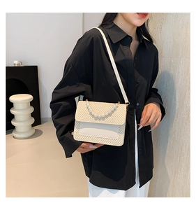 Detail view of woven straw shoulder bag with elegant pearl handle and adjustable strap