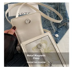 Detail view of white crossbody phone bag featuring golden butterfly embroidery and magnetic snap