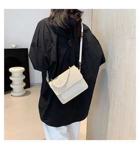 Detailed view of white woven crossbody bag with elegant pearl handle and gold accents