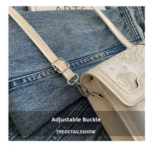 Detail of adjustable silver buckle and metal hook on a white PU leather crossbody bag