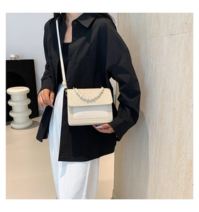 Detail of a beige woven crossbody bag with elegant pearl top handle worn by a model