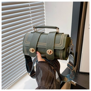 Détail du sac cylindrique vert foncé avec clous dorés et bandoulière ethnique