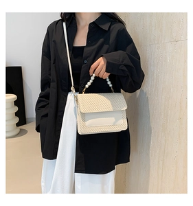 Detail of beige woven flap bag featuring a pearl handle and detachable shoulder strap
