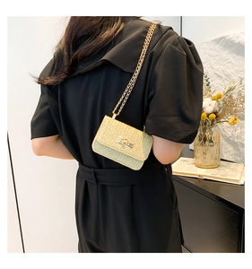 Detail view of woven straw shoulder bag with gold chain strap worn by a model