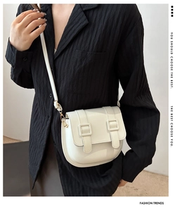Detail of white saddle bag with double buckle straps and adjustable gold metal hardware