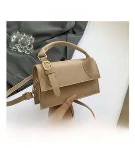 Détail de la texture cuir beige, boucle dorée et logo de marque sur le sac bandoulière