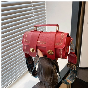 Détail du sac cylindrique rouge avec texture cuir, rivets dorés et fermoirs rotatifs